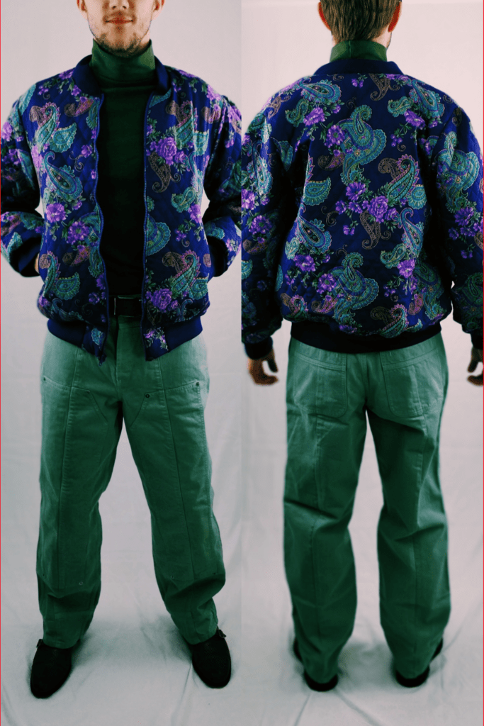 Purple floral/paisley bomber jacket. The model is styled in a green Sweater by top man, green jeans by jacquemus, brown belt by velez and brown shoes.