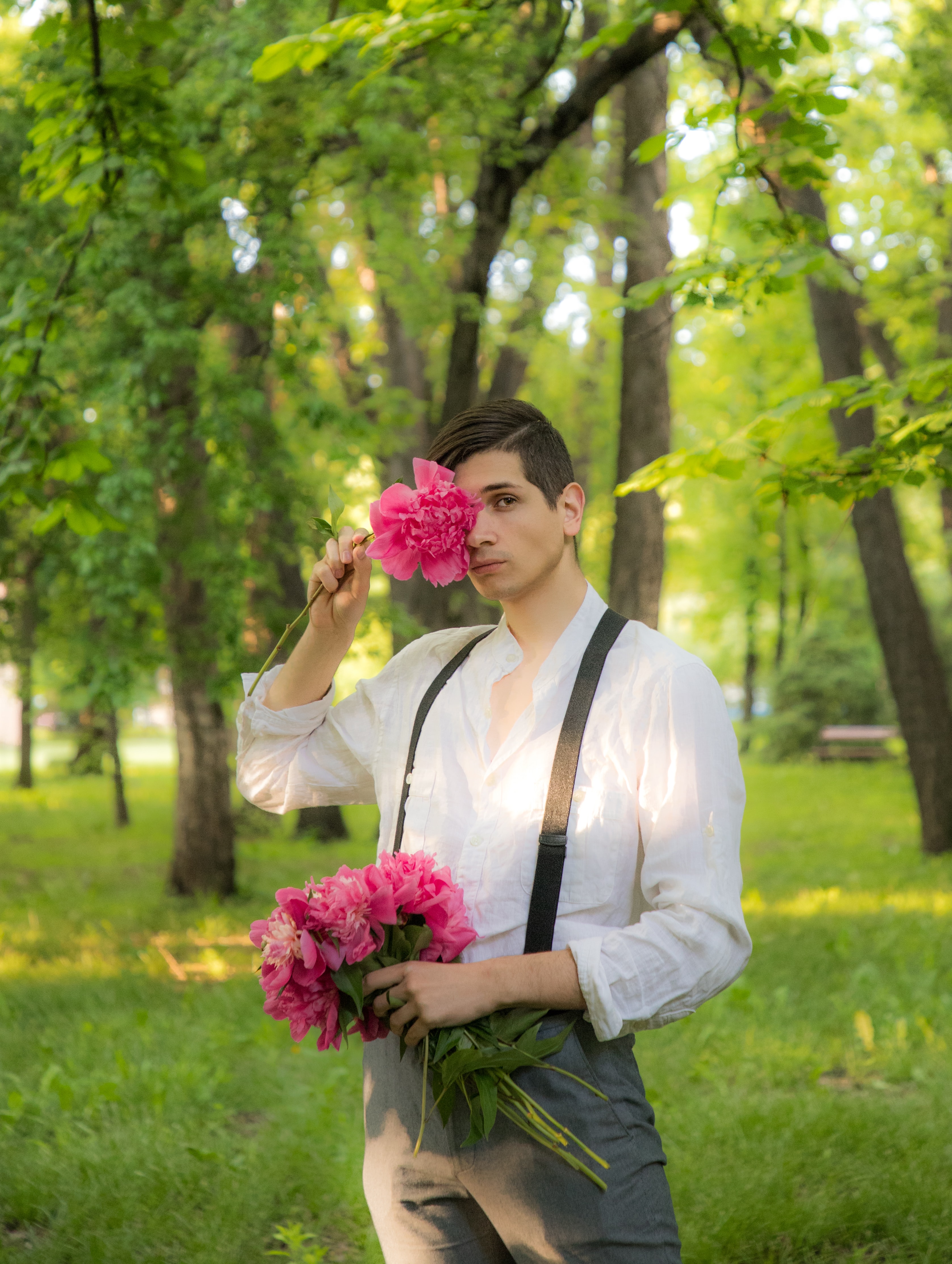 A guy wearing a white shirt, suspenders and pants. He has flowers on his hands. The style is Cottagecore.